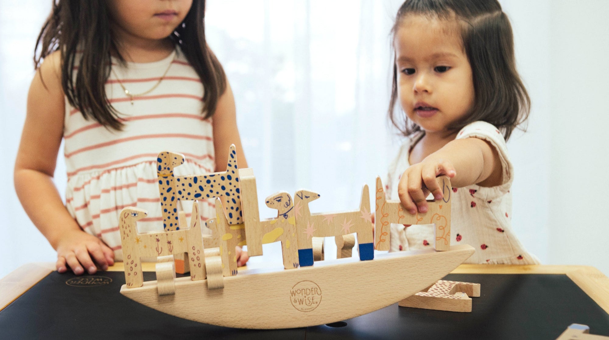 Two kids playing with a balancing wooden animal toy set on a table.