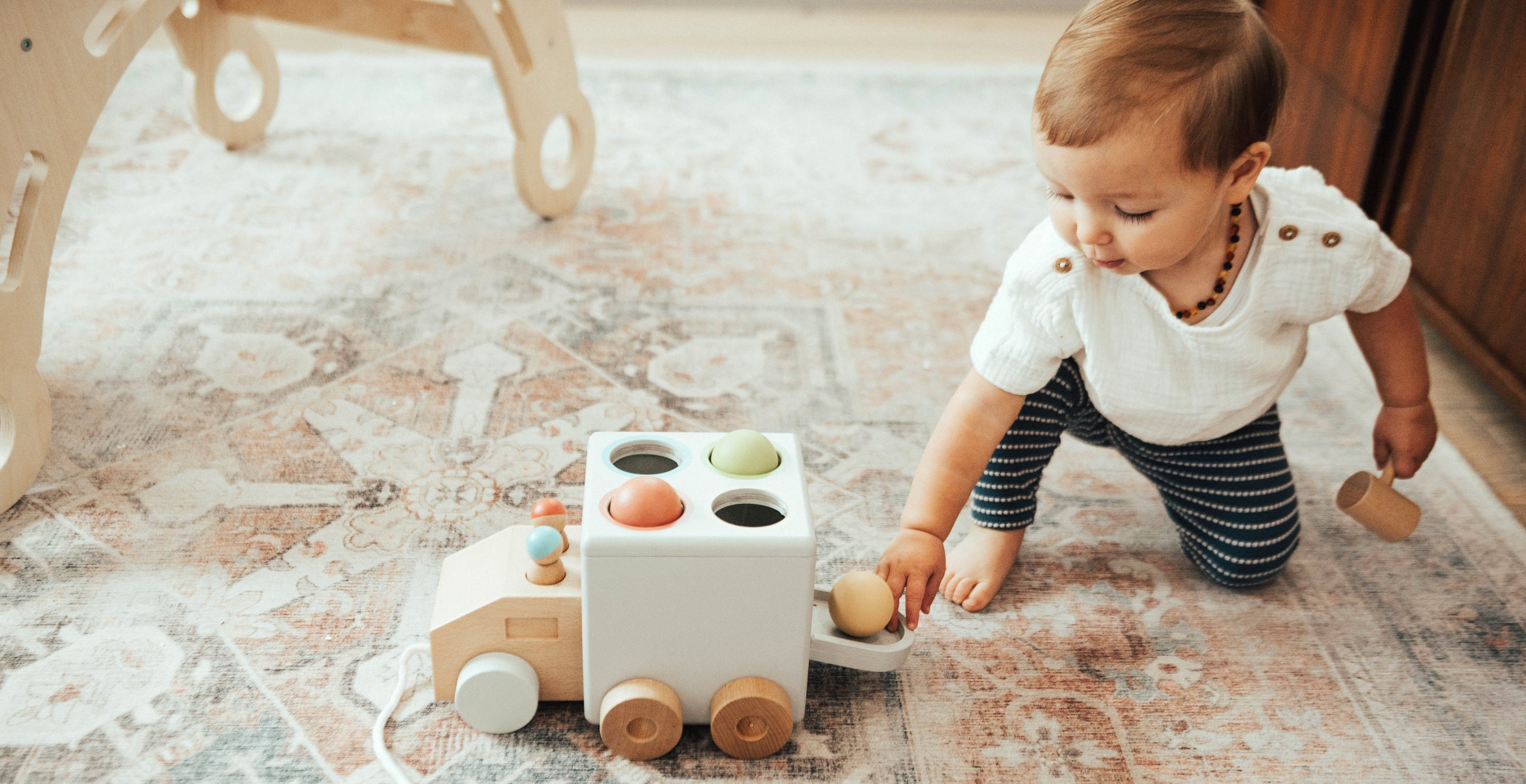 Baby playing with a wooden toy on a patterned rug