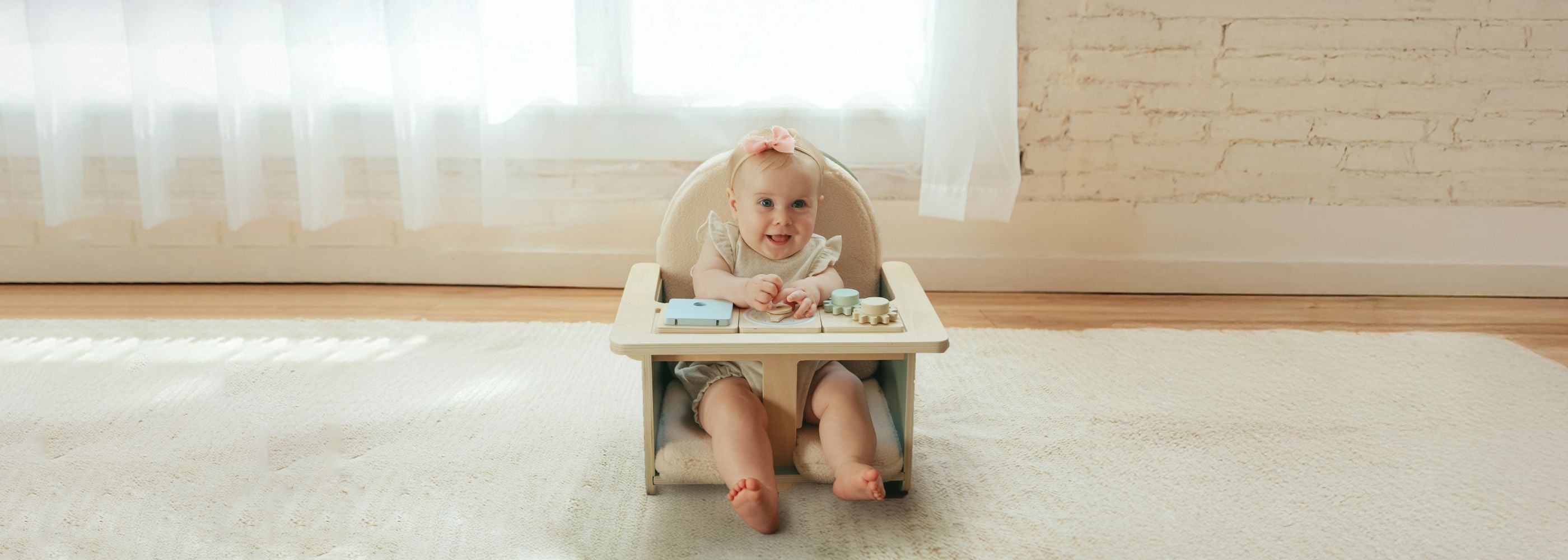 Baby sitting in a wooden chair with toys and a mat for snack time.