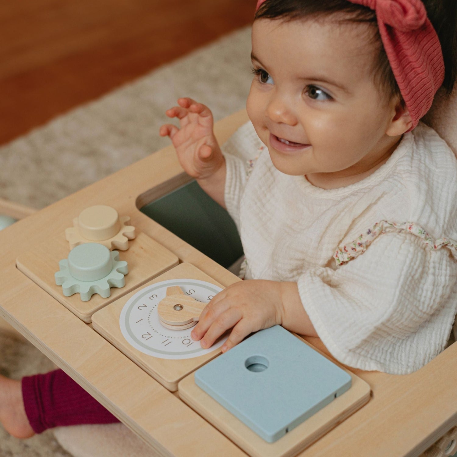 Baby sitting in Little Wood padded wooden chair in nursery, playing with included toys.