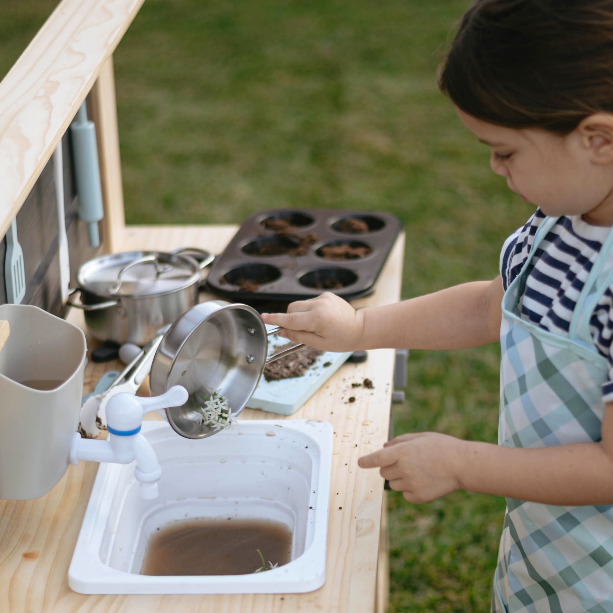 Child using mud kitchen for kids with strainer and water in outdoor play setting