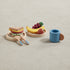 Set of wooden toy picnic basket items including a sandwich, fruit, and a cup on a beige background