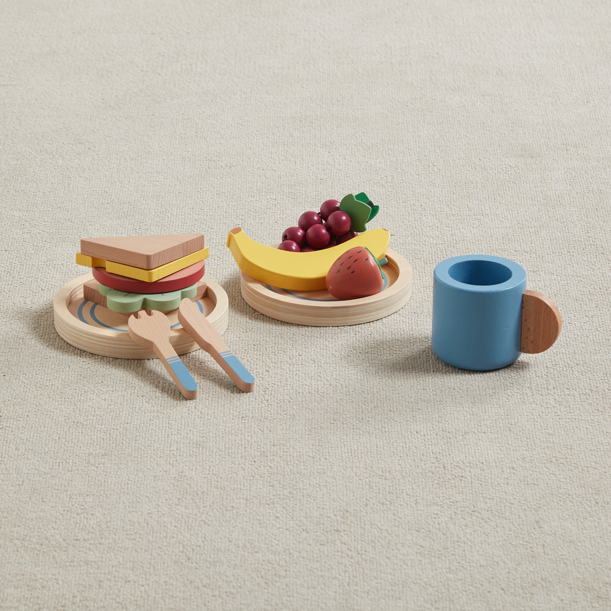 Set of wooden toy picnic basket items including a sandwich, fruit, and a cup on a beige background