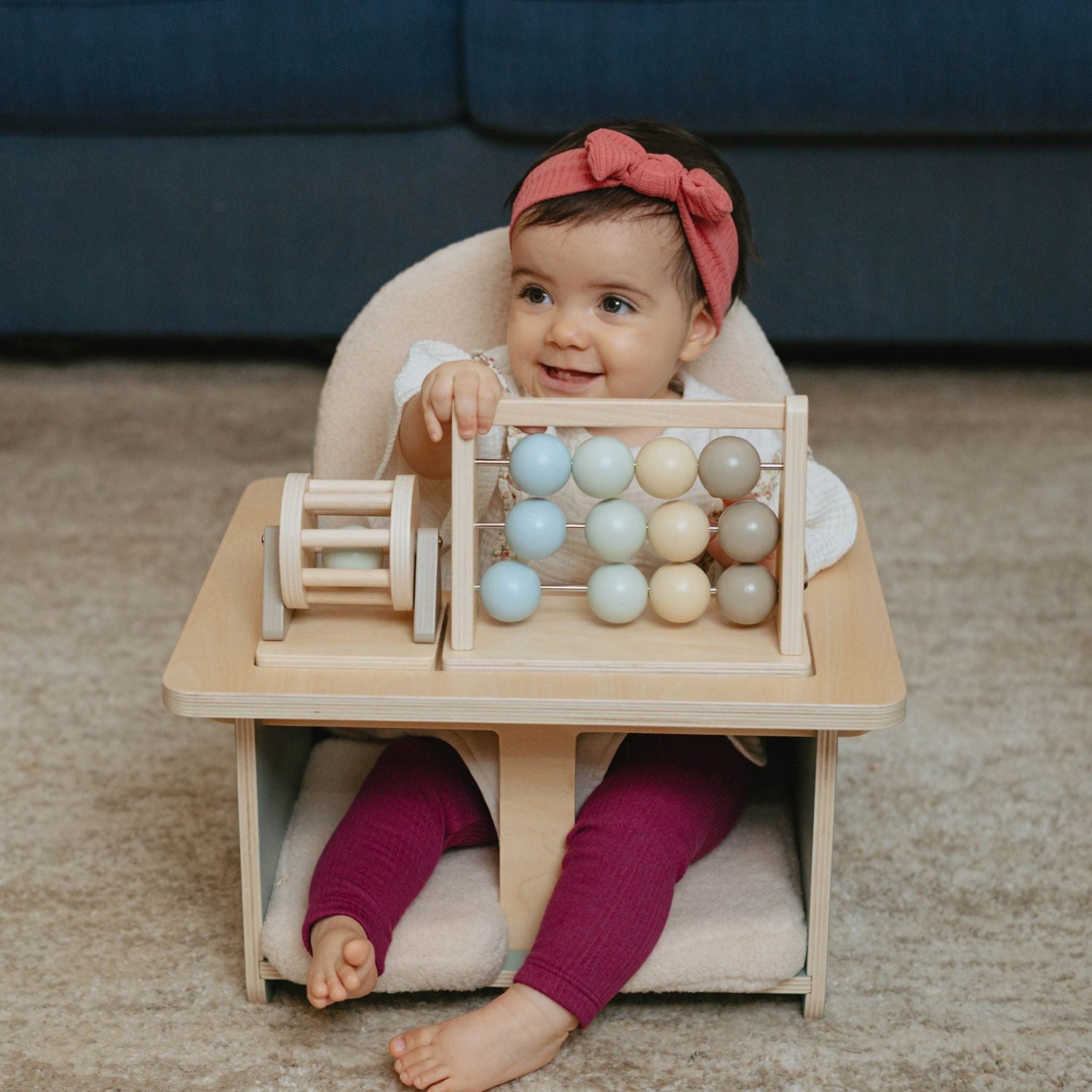 Child playing with a wooden abacus toy sitting in the supportive baby activity chair designed for sitting, playing, and snack time.