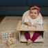 Child sitting in a small wooden chair exploring five interchangeable educational toys: an abacus, spinning gears, peek-a-boo mirror, rotating ball cage, and clock.
