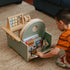 Child organizing books and toys in the storage compartment of the little wood baby activity chair.