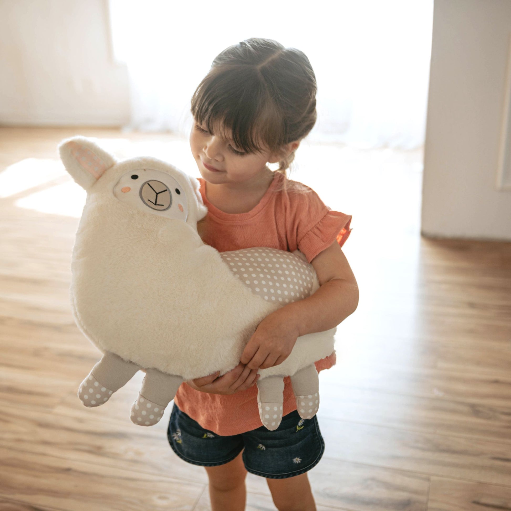 Young child holding cream-colored llama stuffed animal in bright room