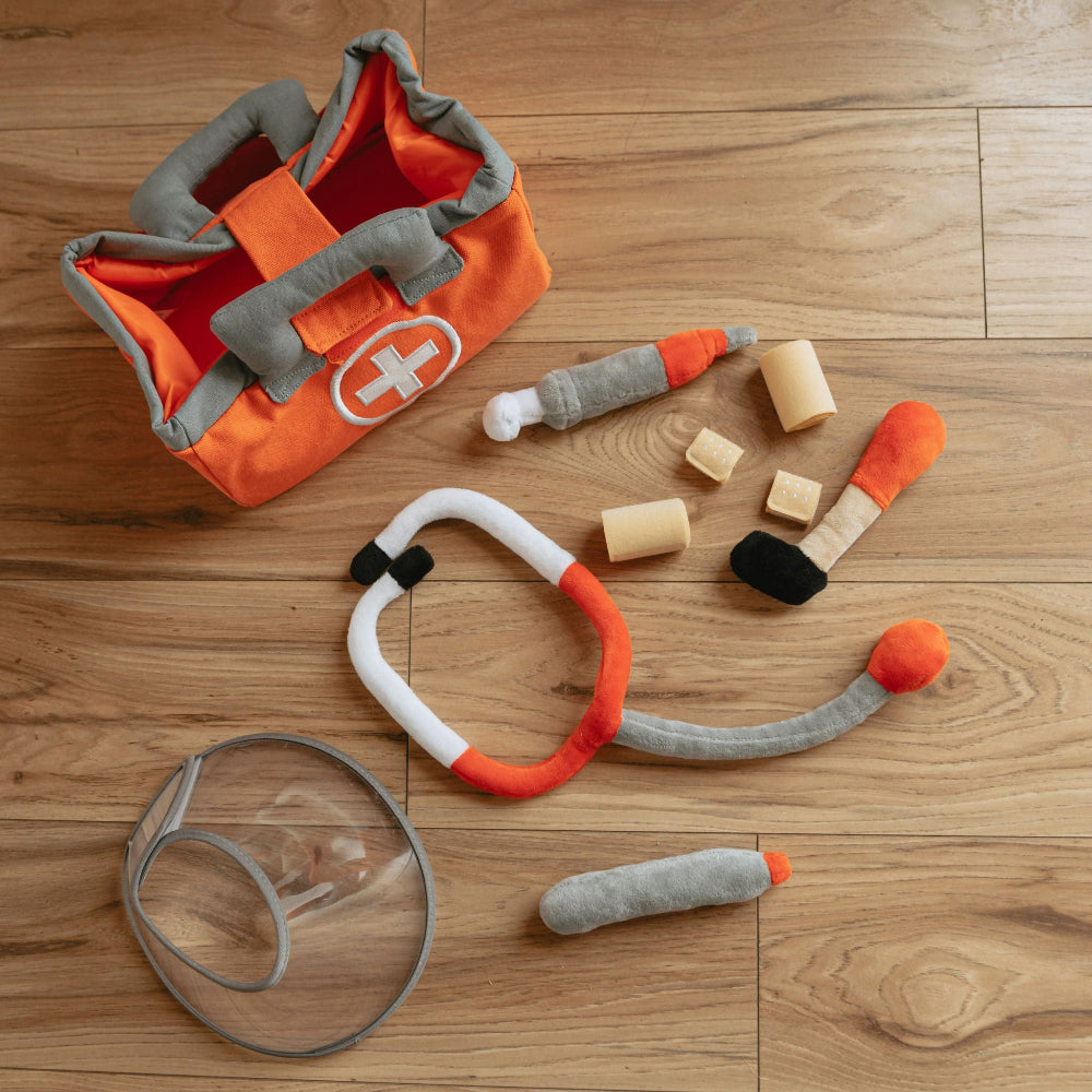 Pretend pet vet play set for kids with plush stethoscope, bandages, thermometer and orange canvas carry bag on a wood floor
