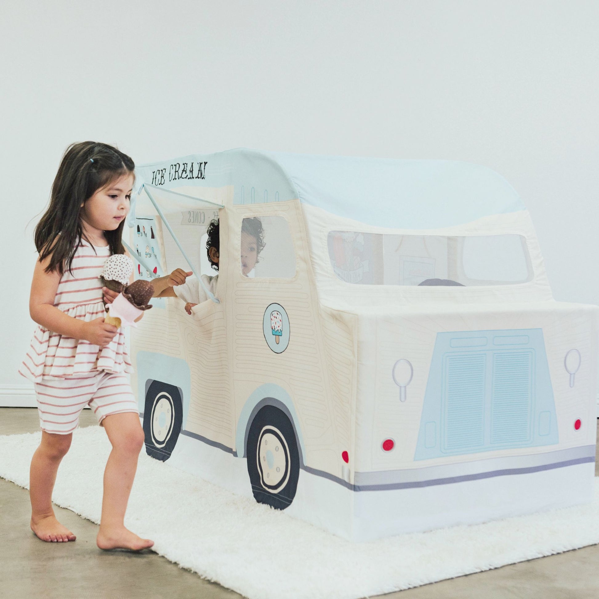 Young girl playing with ice cream truck playhouse, holding ice cream cone toy