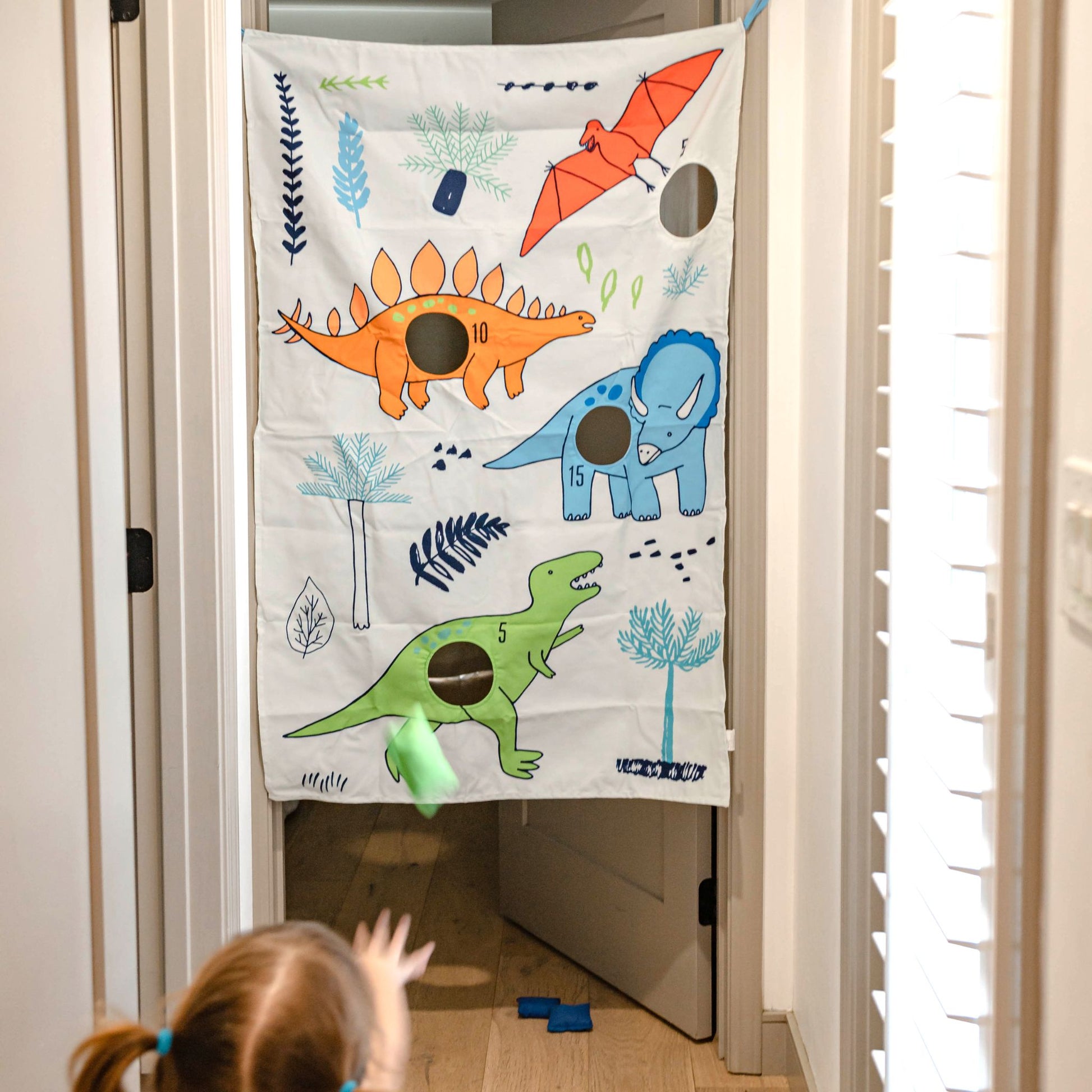 Child playing with dinosaur doorway bean bag toss game featuring colorful dino graphics