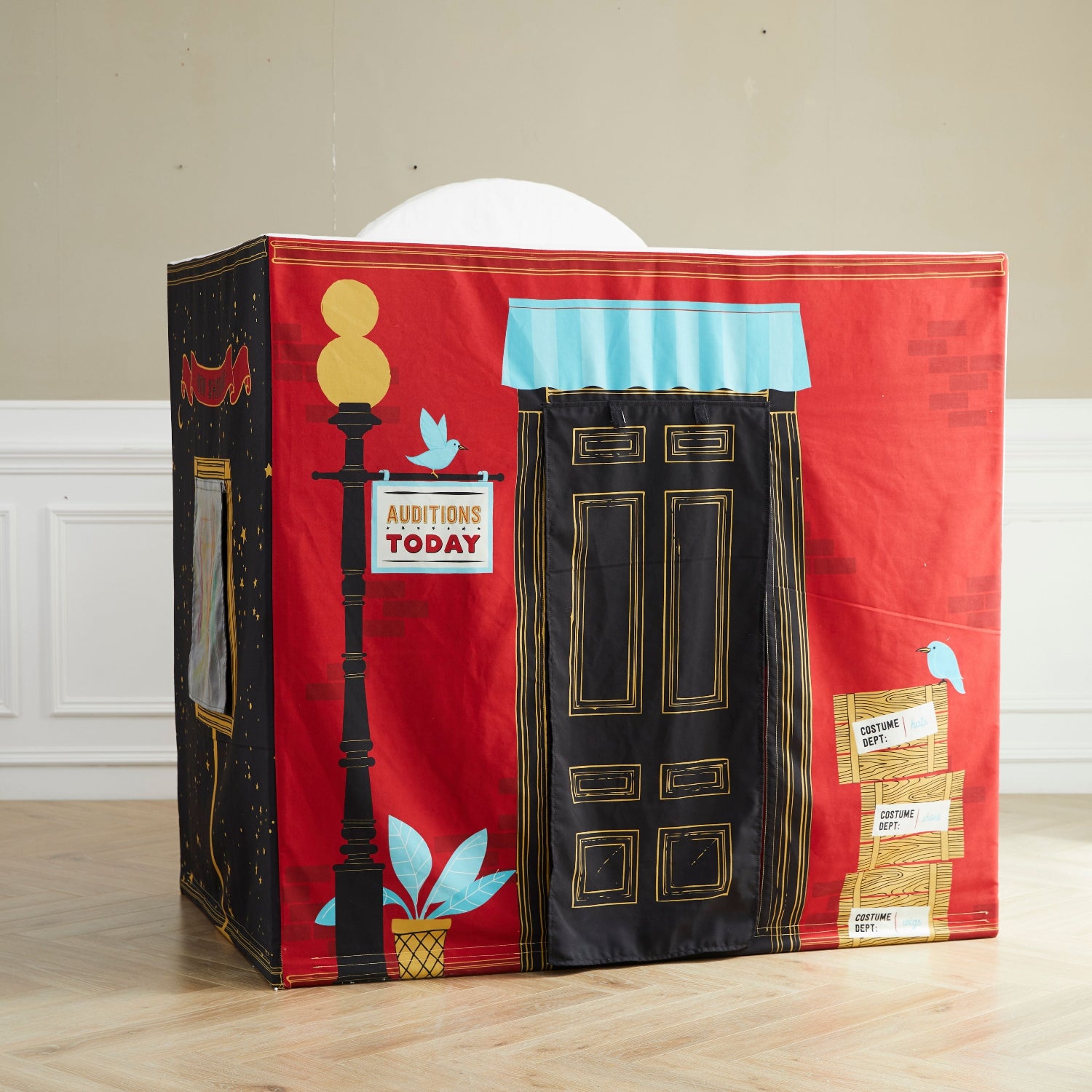 Back of kid's playhouse is painted red with black door and blue accents on a wooden floor.