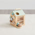 Wooden activity cube for toddlers with pastel rings, beads, and birdhouse top on white surface
