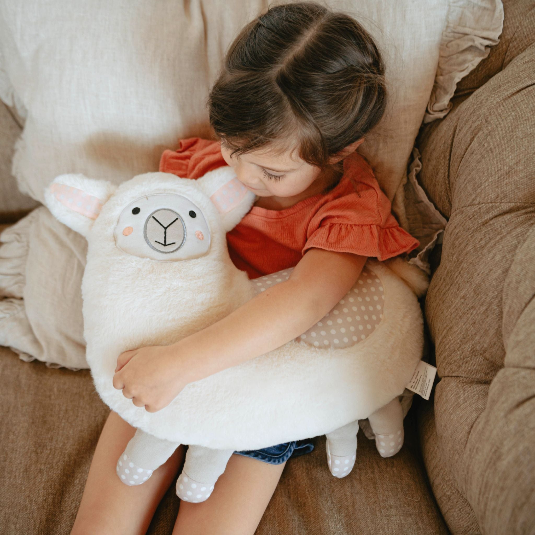 Toddler hugging white llama stuffed animal on couch wearing red shirt