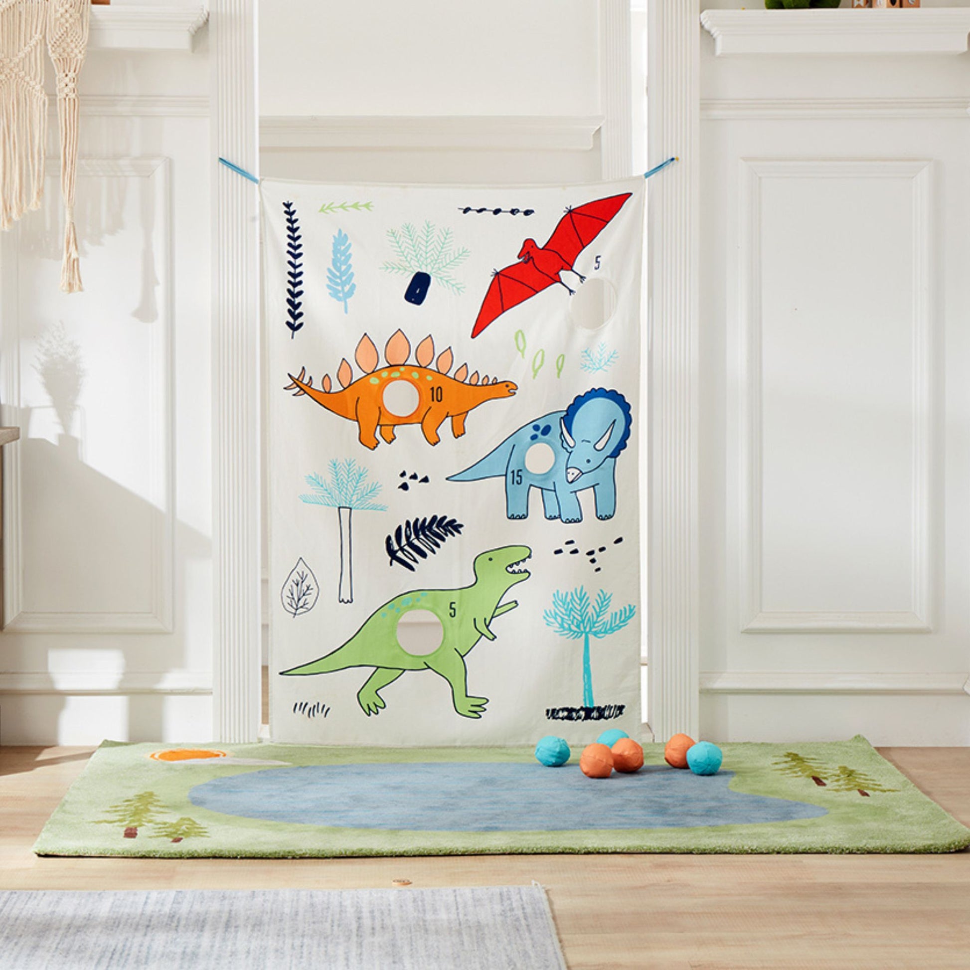Dino Doorway Bean Bag Toss game hung between white doors with colorful dinosaur and plant designs, balls scattered on green play mat