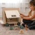 Child playing with a wooden dollhouse and accessories on a carpeted floor.