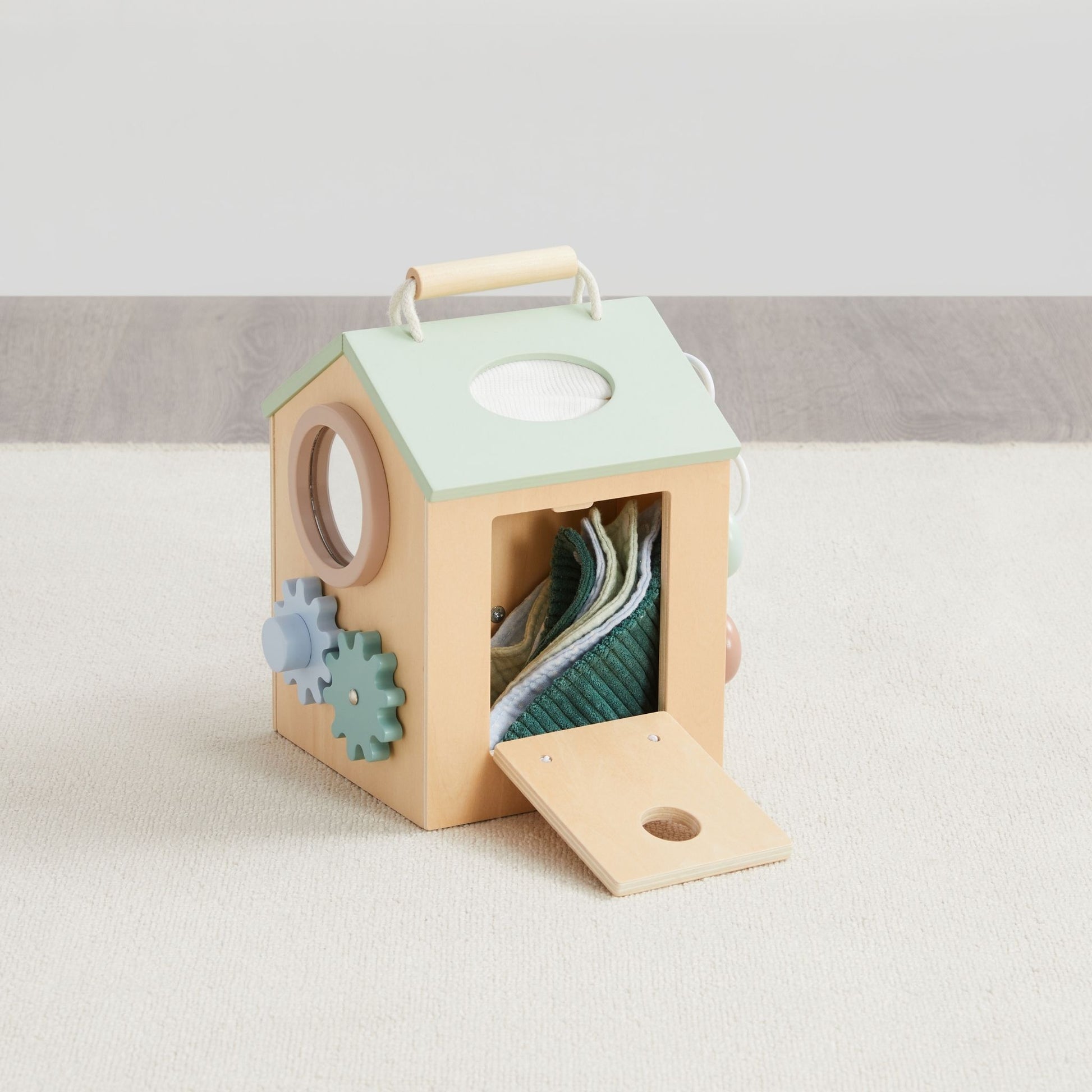 Wooden activity cube for toddlers with mint green roof, natural wood finish, and fabric storage visible through open door