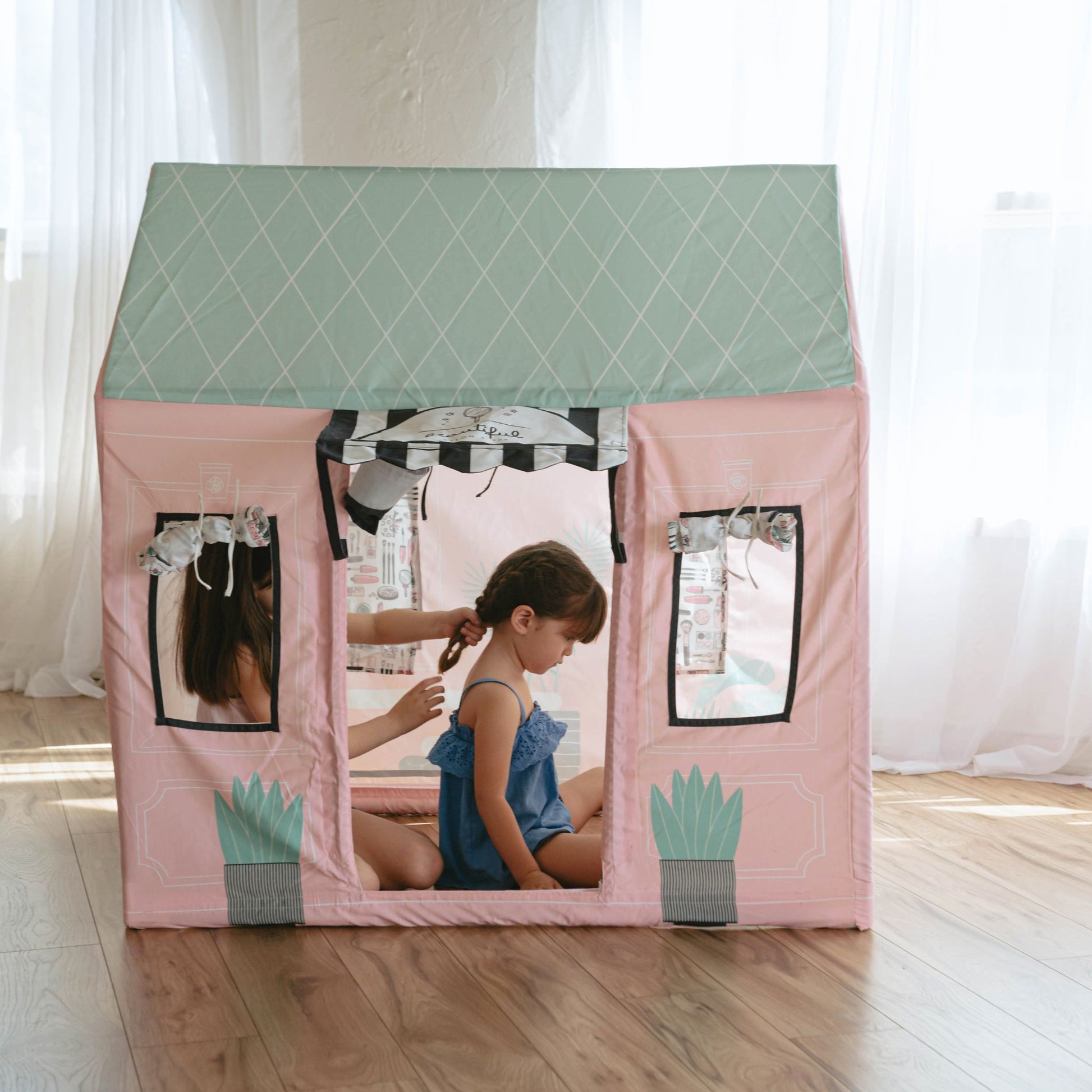 Girl playing inside pink kids play tent beauty salon with green roof and window details