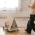 Person pulling a small wooden house toy on wheels across a wooden floor.