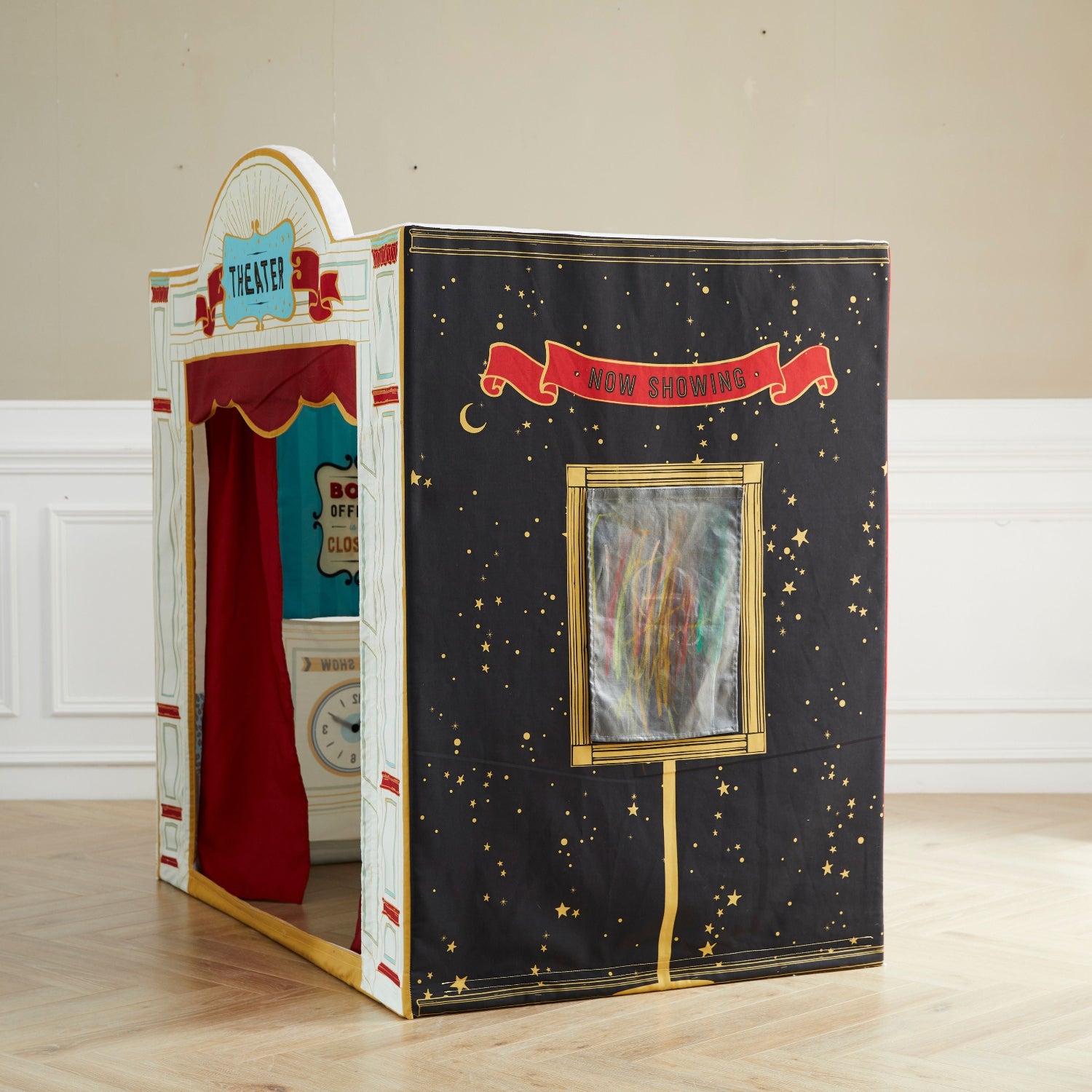 Children's playhouse with a red curtain and 'Now Showing' sign on a wooden floor.