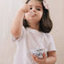 Toddler girl playing with pink plush tea set, blowing bubble while holding toy teacup