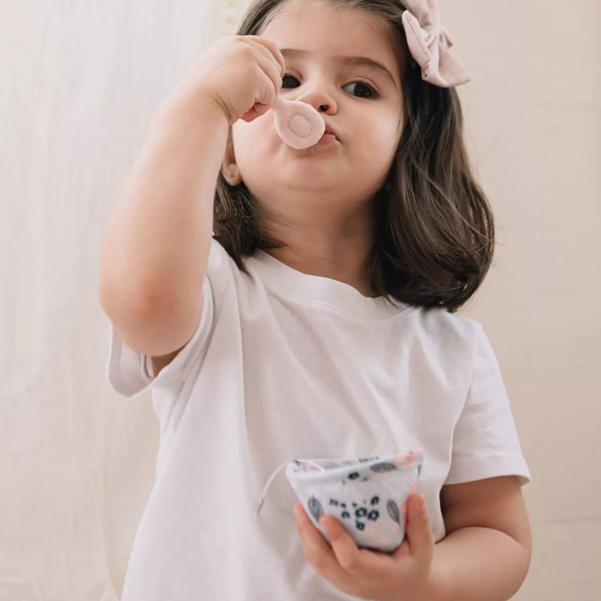 Toddler girl playing with pink plush tea set, blowing bubble while holding toy teacup
