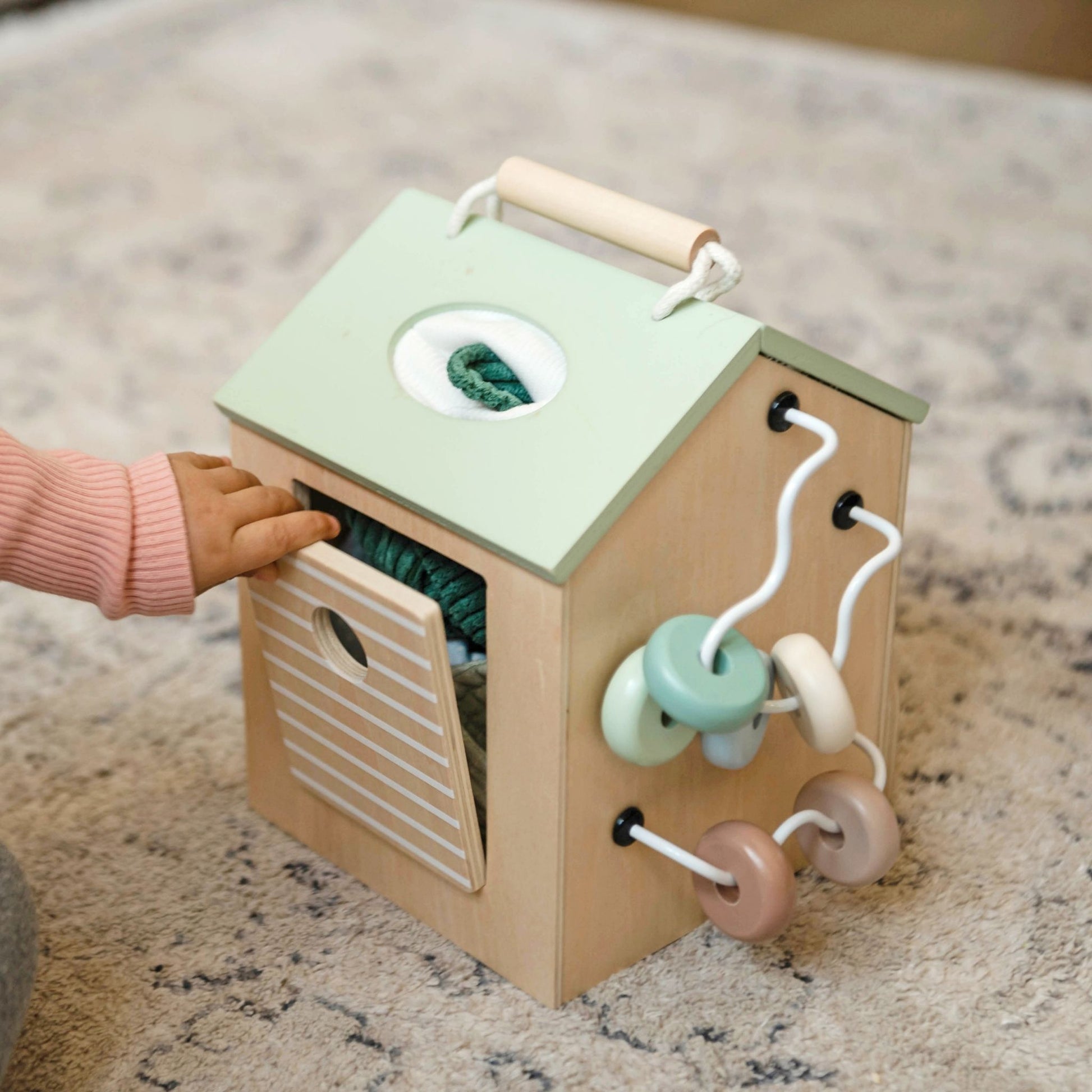 Toddler playing with wooden activity cube featuring mint green roof and interactive bead toys