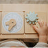 Child's hand interacting with a wooden toy clock and gears on a wooden surface of baby wood chair.