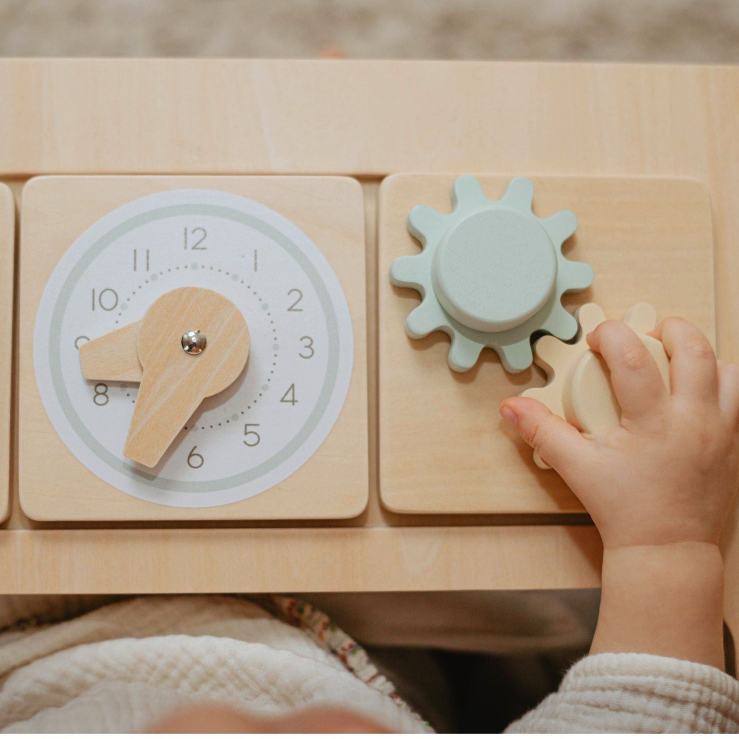 Child's hand interacting with a wooden toy clock and gears on a wooden surface of baby wood chair.