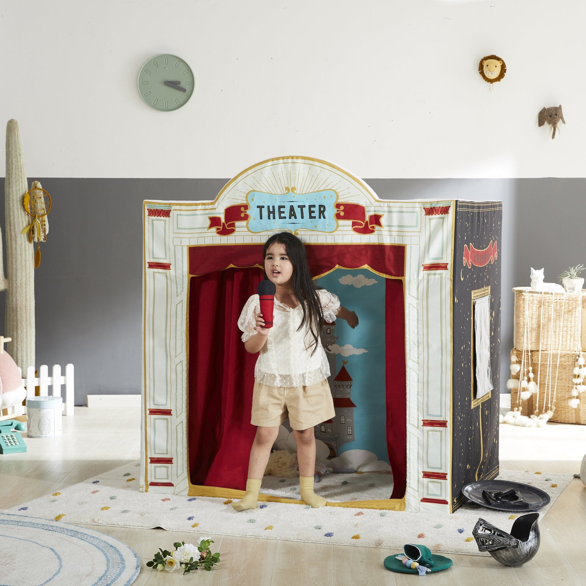 Child holding a red microphone on the Play House Playhouse stage with the castle backdrop, in a playroom