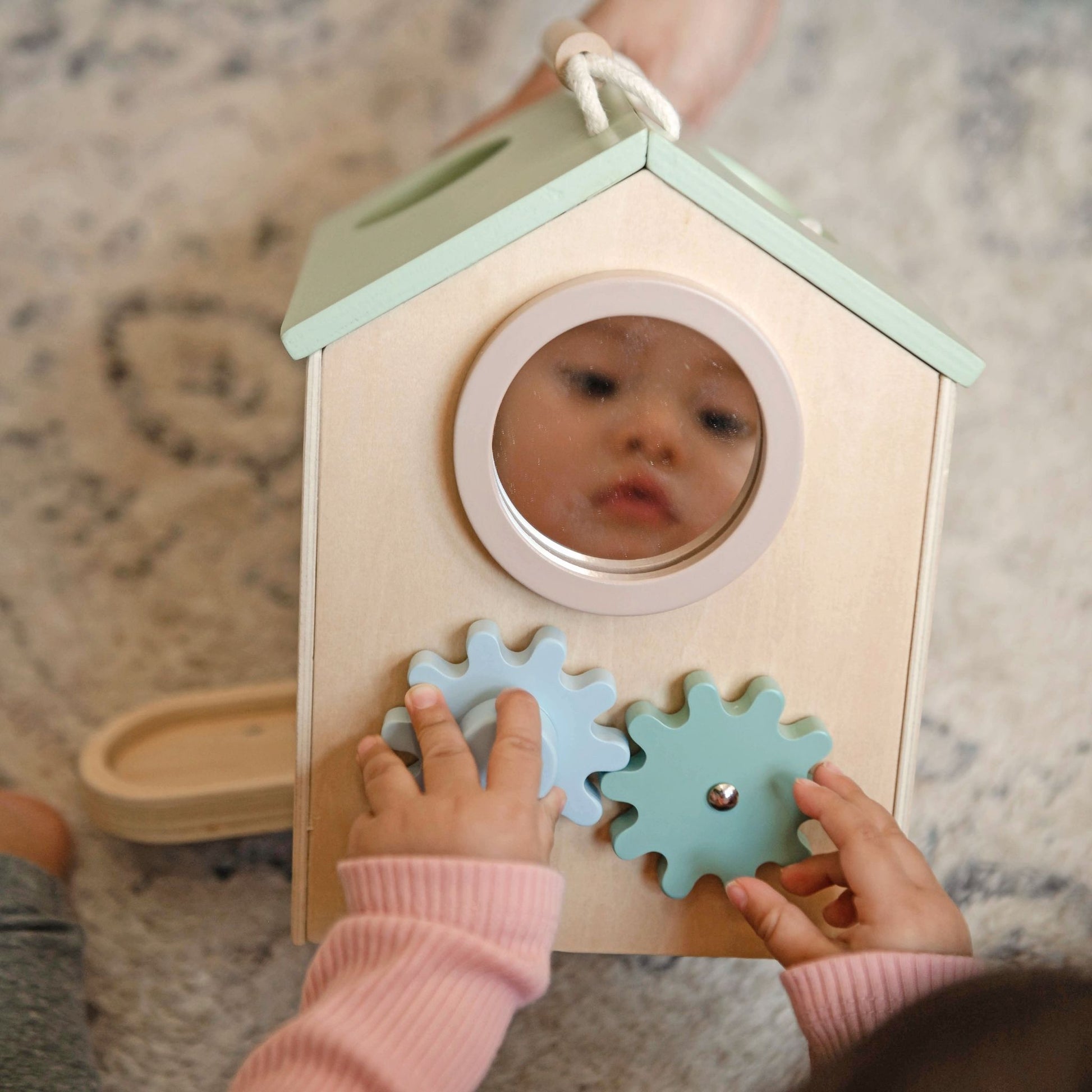 Toddler playing with wooden activity cube featuring mirror and gear toys in pastel colors