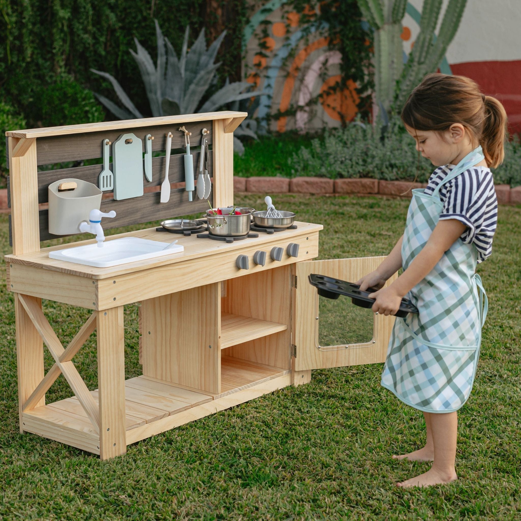 Child playing with wooden mud kitchen for kids in backyard garden setting