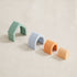 Colorful silicone arch toys in mint, gray, orange and peach displayed in a row on a neutral surface