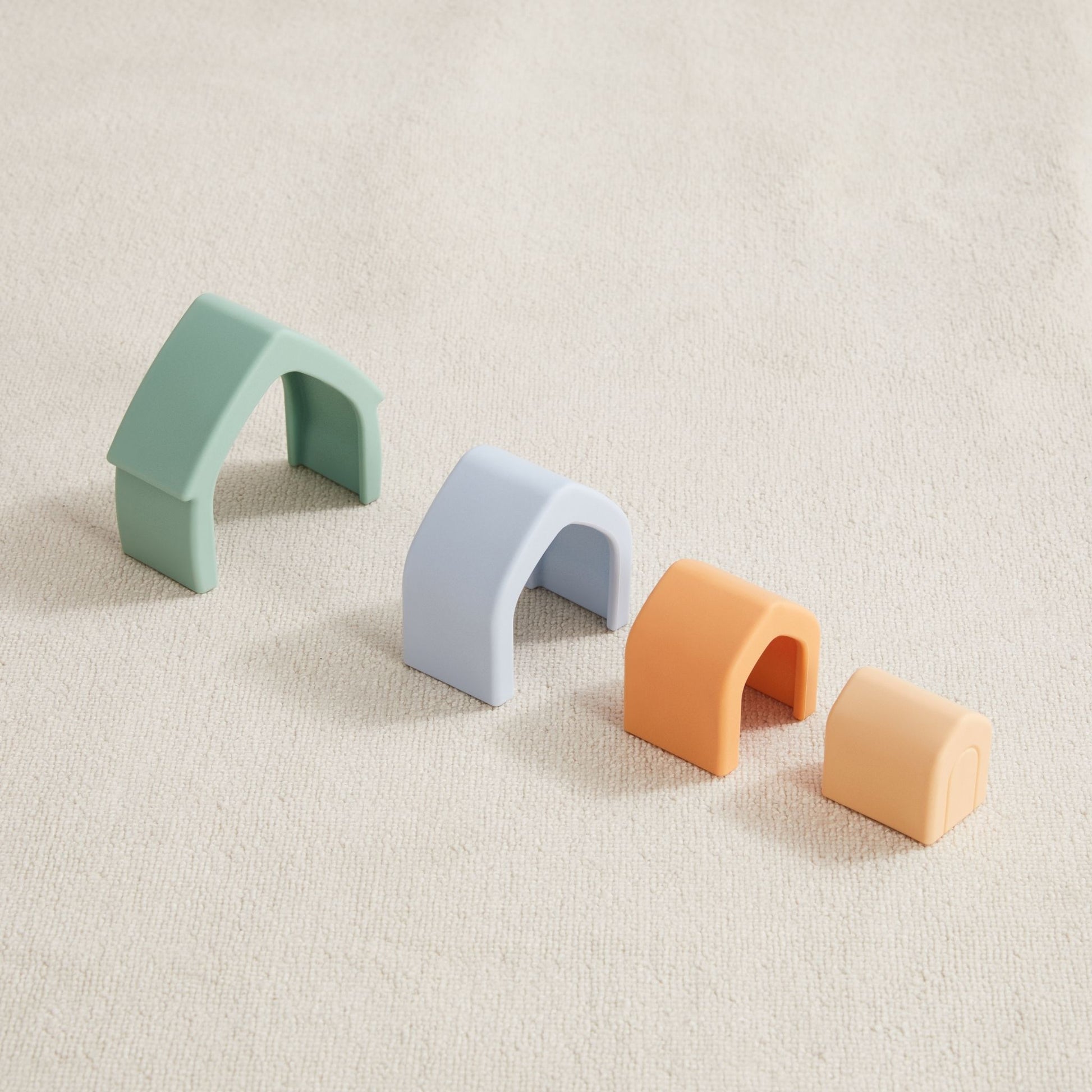 Colorful silicone arch toys in mint, gray, orange and peach displayed in a row on a neutral surface