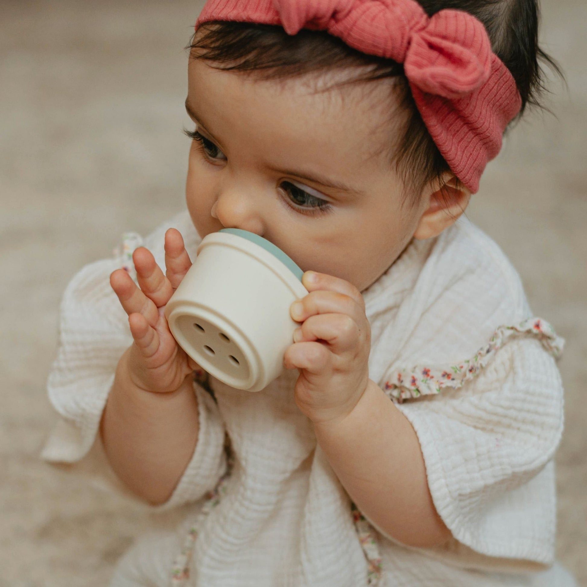 Baby girl wearing pink bow drinking from white sippy cup from 9-12 month gift set