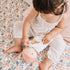 Toddler on a floral quilt swaddling the Cookie Baby Bundle Doll.