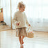 Child walks across a wooden floor carrying the Doll Carrier by its rope handles with a plush bottle in hand