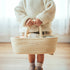 Close-up of a child's hands gripping the rope handles of the Doll Carrier, doll and bottle inside