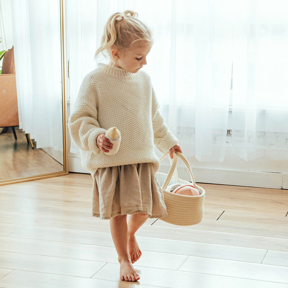 Child carries the Doll Carrier and Bundle Baby Sweet Pea carrier by its handles, doll inside and bottle in hand