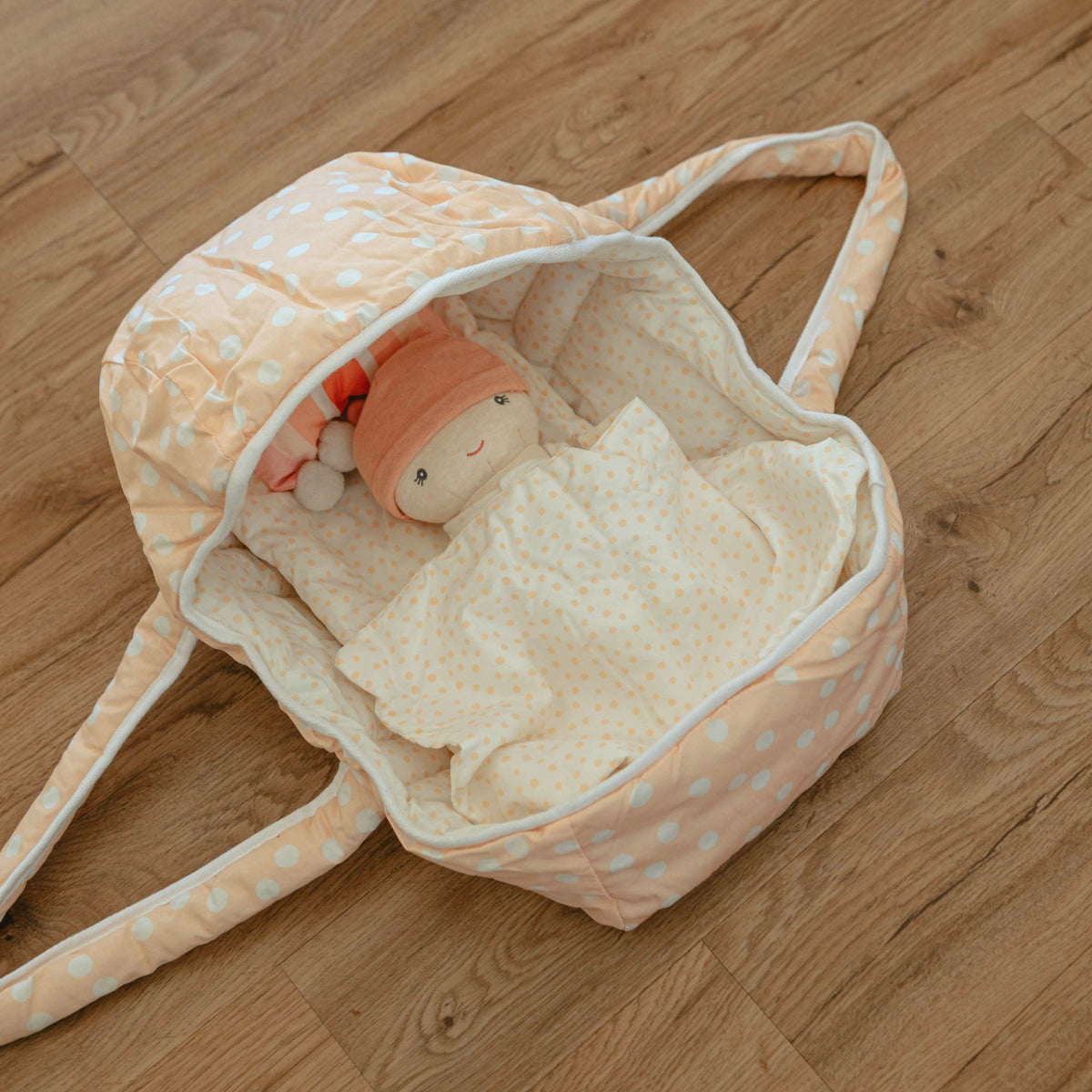 Dots and Rainbows Doll Carrier on a wood floor with the Cookie doll tucked under the blanket inside