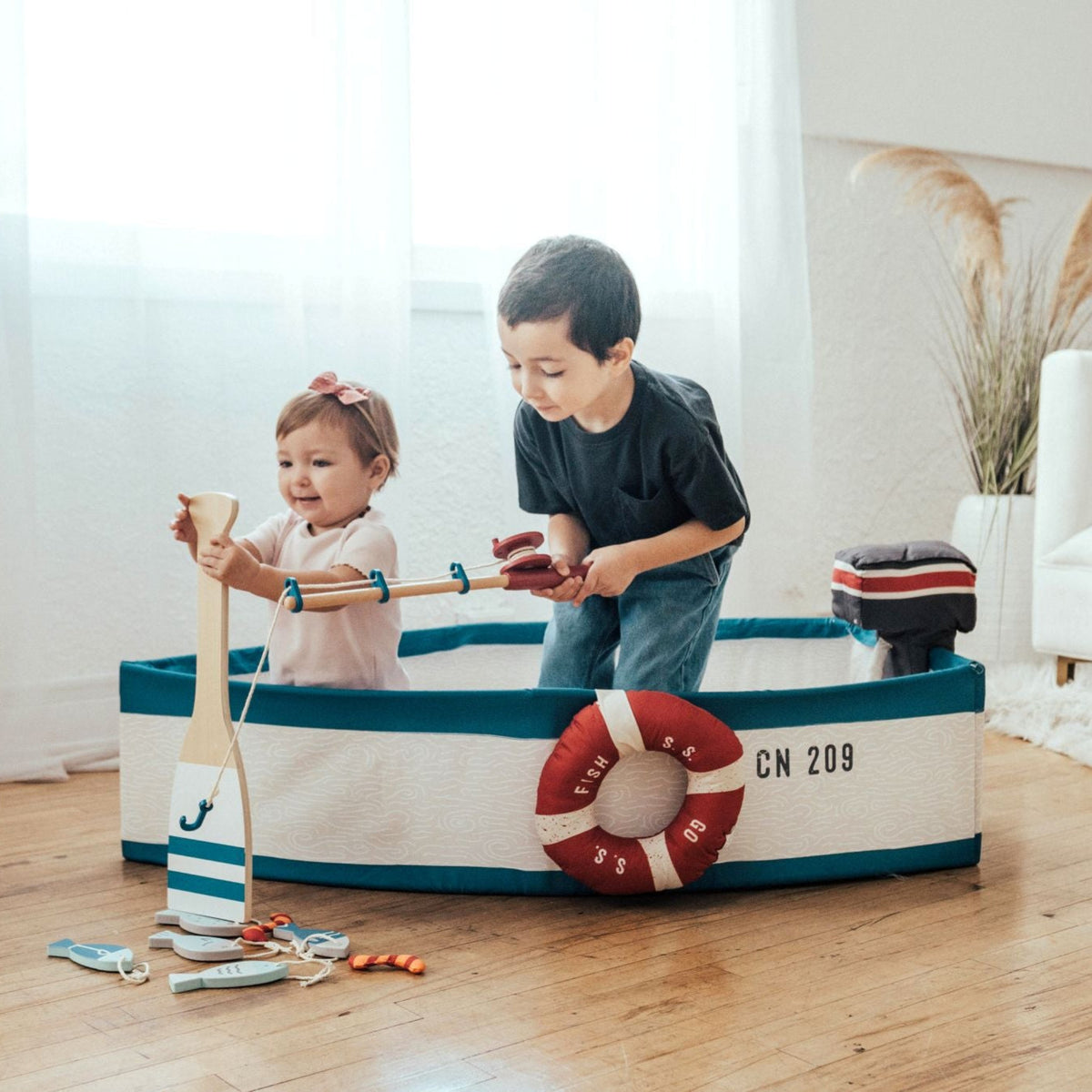 Two children fishing from the Gone Fishing Boat on a wood floor by a bright window