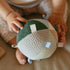 Baby hands holding Hello Baby 6-9 month gift set with green and cream colored items in woven basket