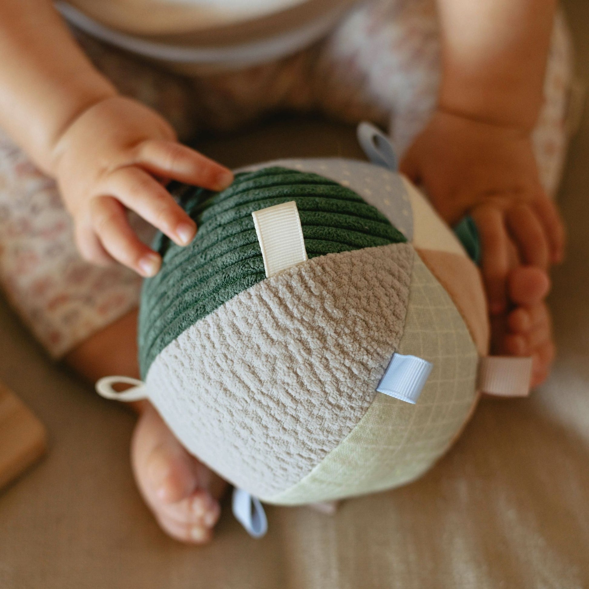 Baby hands holding Hello Baby 6-9 month gift set with green and cream colored items in woven basket