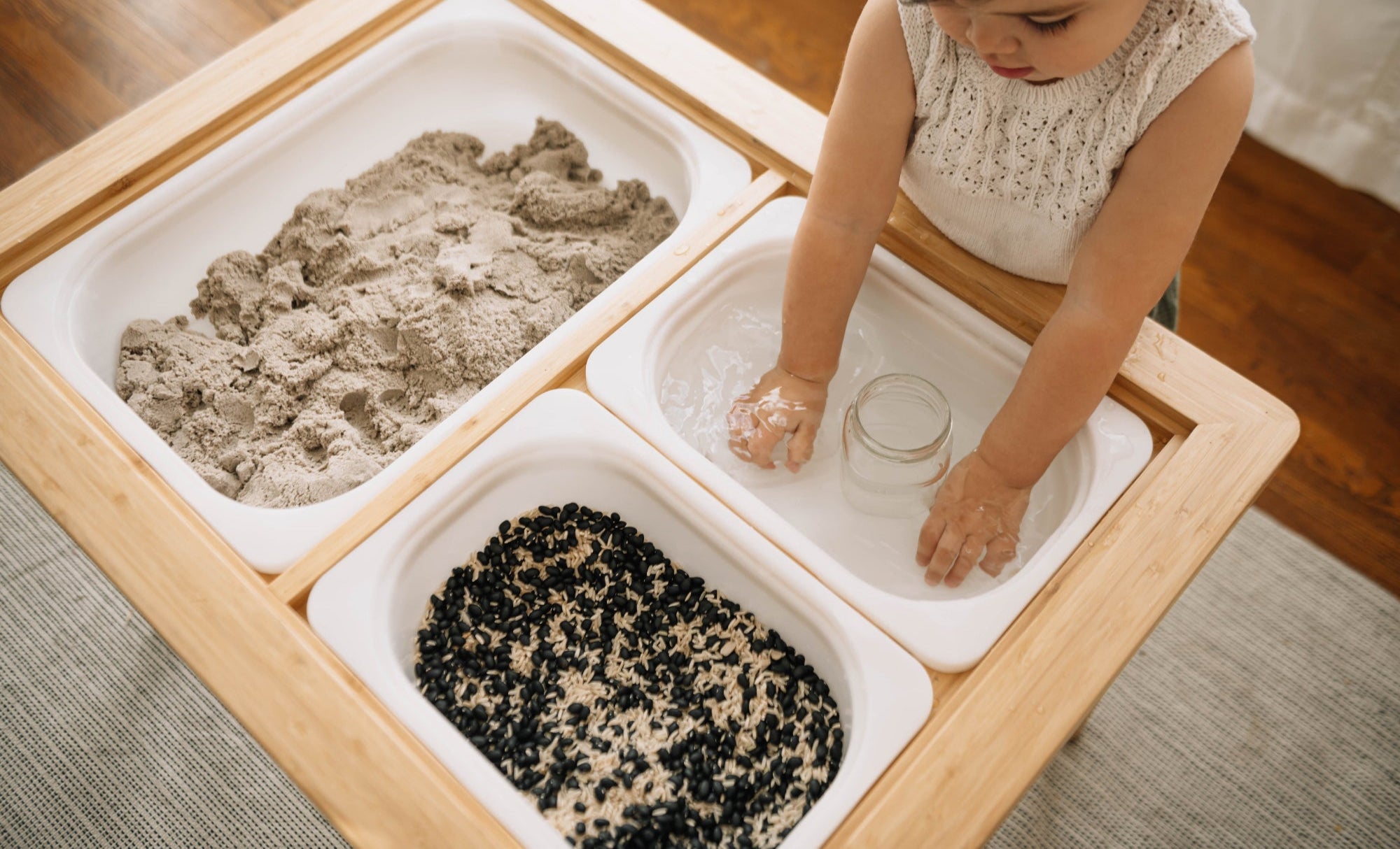 Child playing with sand and water in a wooden sensory table.