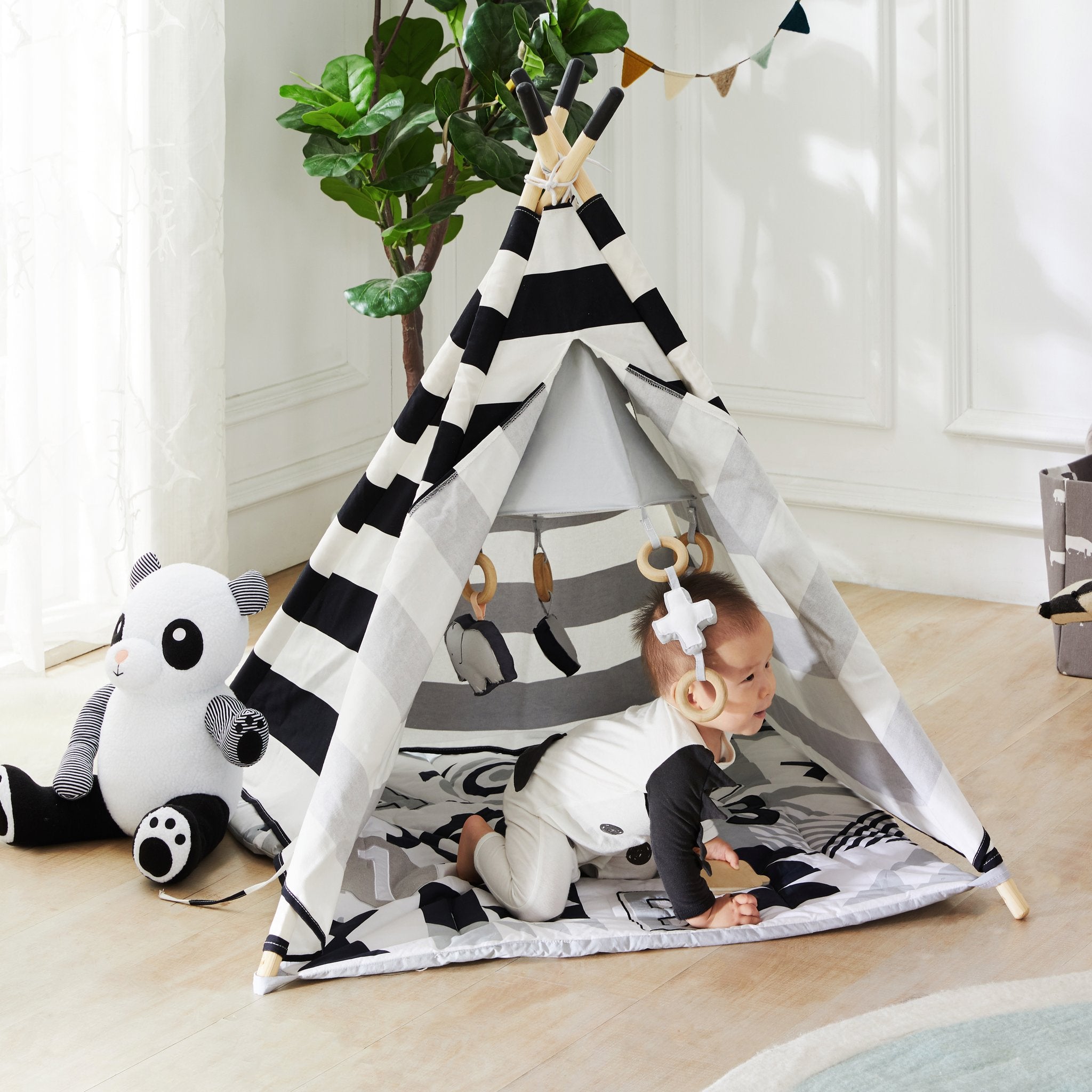 Baby crawling inside the ABC Baby Activity Teepee next to a panda plush on a wood floor