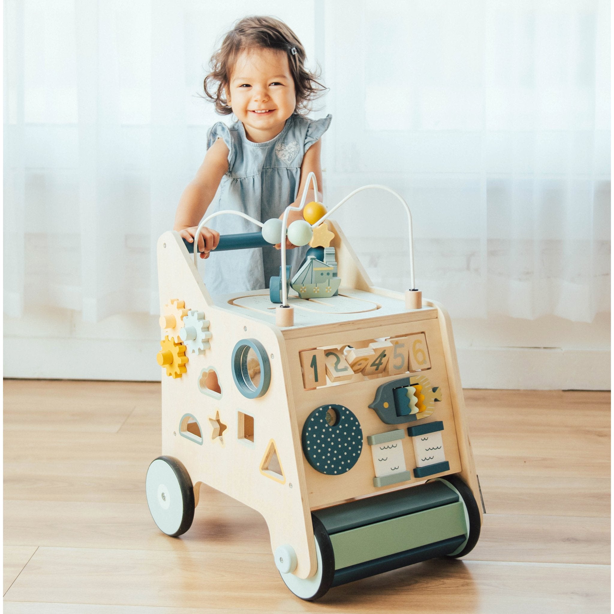 Toddler smiling while pushing the Busy Busy Activity Walker across a wood floor