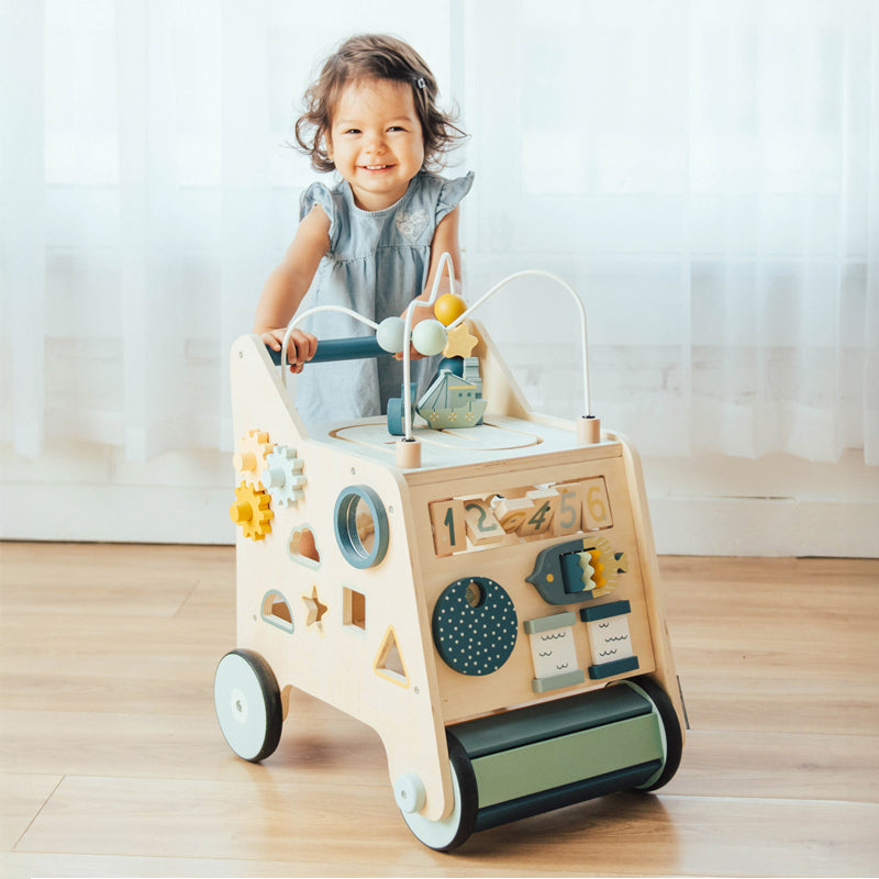 Toddler girl with a Busy Busy Activity Walker, a wooden push walker toy