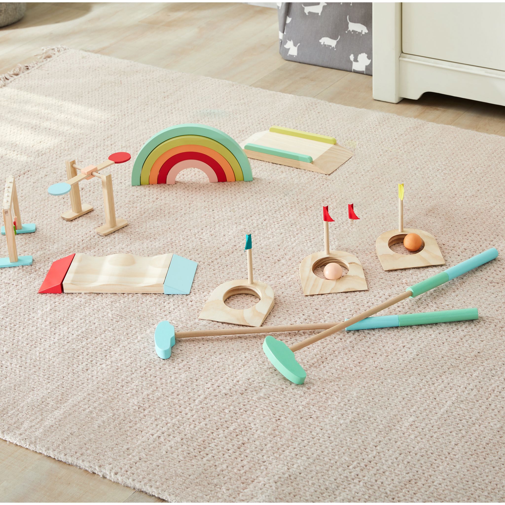 Good Wood Mini Golf Game set on white: three wooden holes with teal, red and yellow flags, two putters with pastel grips, two wooden balls, rainbow tunnel, bead curtain, spinner, flat bridge and wavy bridge