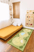 A green and beige golf course themed rug on a hardwood floor in a child's bedroom, next to a daybed with a yellow cover and a wooden climbing wall.