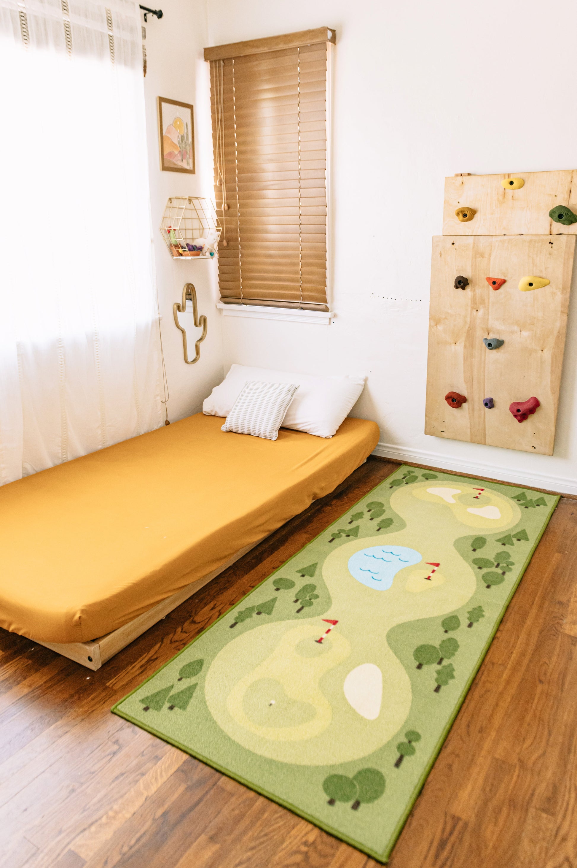 A green and beige golf course themed rug on a hardwood floor in a child's bedroom, next to a daybed with a yellow cover and a wooden climbing wall.