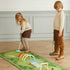 Two children playing with a golf set on a green mat indoors.